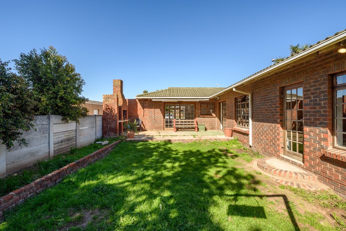 A rear garden featuring a brick braai, concrete patio area, and established lawn, enclosed by a precast concrete boundary wall.