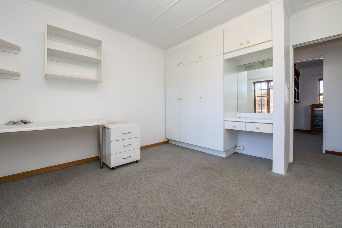 A clean, neutral bedroom featuring extensive built-in cabinetry, a vanity area with mirror, and wall-mounted shelving, offering a functional and versatile living space.