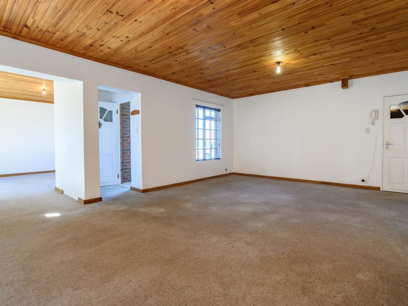 Spacious, empty living area featuring a warm timber tongue and groove ceiling, neutral walls, and carpeted flooring, offering a versatile blank canvas.