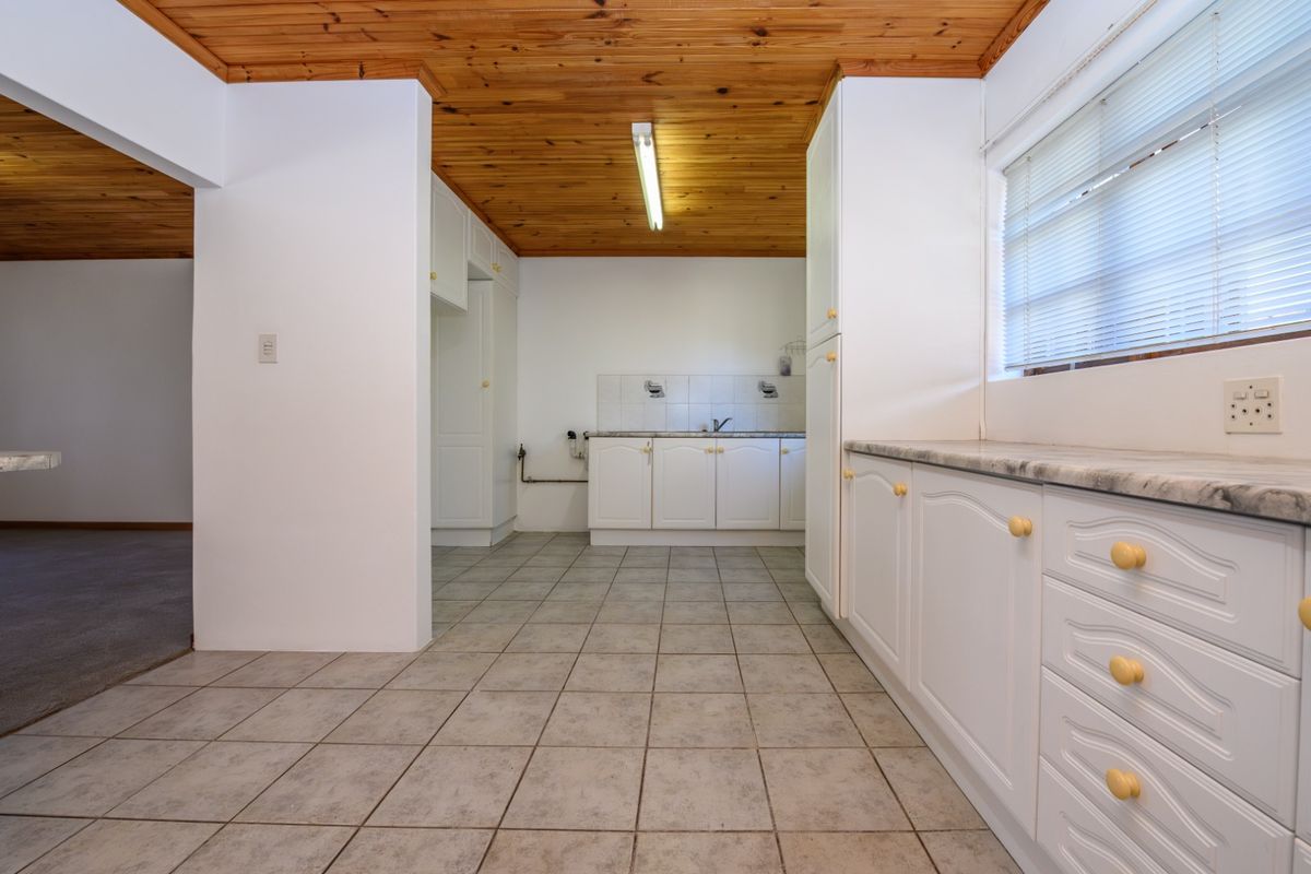 A functional kitchen featuring white built-in cabinetry, laminate countertops, tiled flooring, and a timber-clad ceiling, offering a clean and practical workspace.