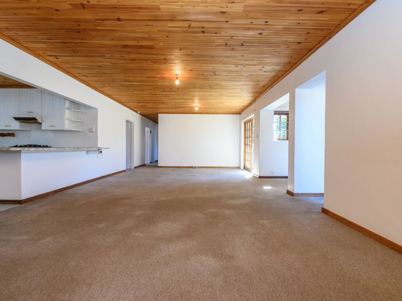 Spacious open-plan living area featuring a timber ceiling, neutral walls, and an integrated kitchen with stone countertops, leading to an outdoor patio area.