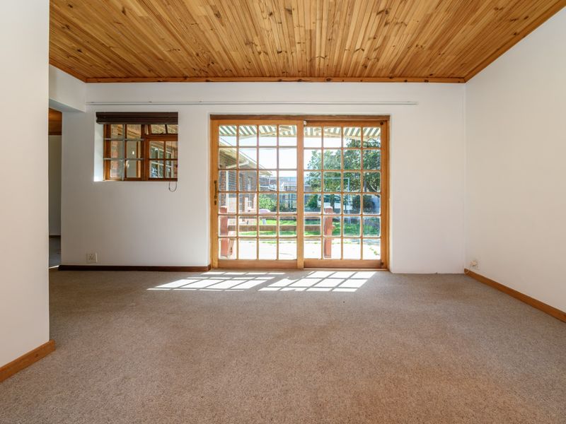 An empty living room featuring a timber tongue and groove ceiling, carpet flooring, and sliding glass doors providing access to the rear garden.