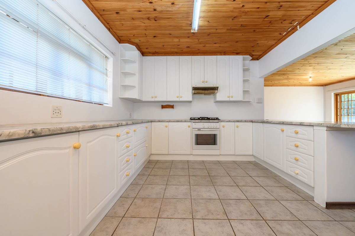 A functional kitchen featuring white cabinetry, marble-look countertops, built-in oven, gas hob, and a distinctive timber ceiling, offering a clean and practical workspace.