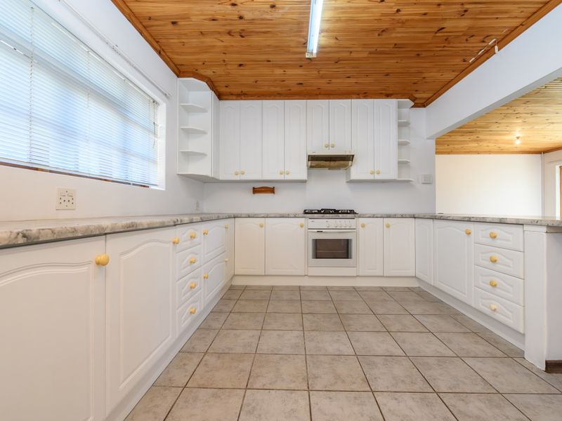 A functional kitchen featuring white cabinetry, marble-look countertops, built-in oven, gas hob, and a distinctive timber ceiling, offering a clean and practical workspace.