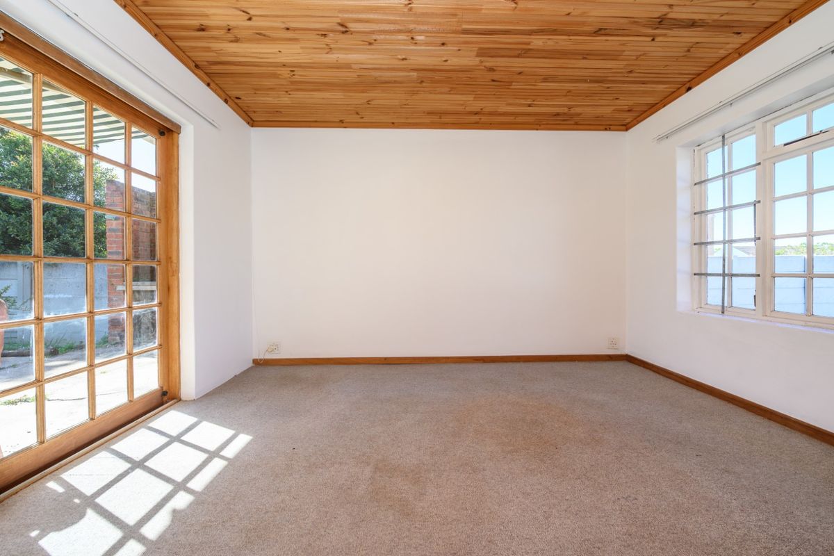 An empty bedroom featuring a timber-clad ceiling, carpeted flooring, and natural light through a wooden-framed sliding door and window.