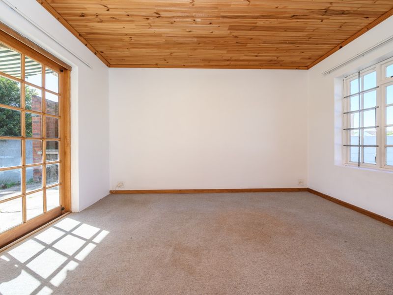 An empty bedroom featuring a timber-clad ceiling, carpeted flooring, and natural light through a wooden-framed sliding door and window.