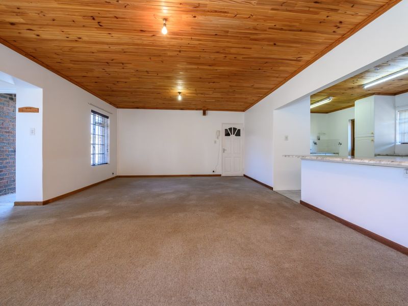 Spacious open-plan living area featuring a timber tongue and groove ceiling, carpeted flooring, and a breakfast bar connecting to the kitchen.