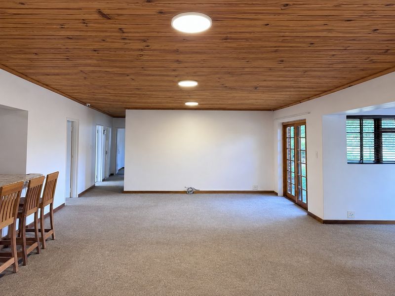 Spacious open-plan living area featuring a warm timber ceiling, neutral carpeting, and direct access to the outdoors through wooden french doors.