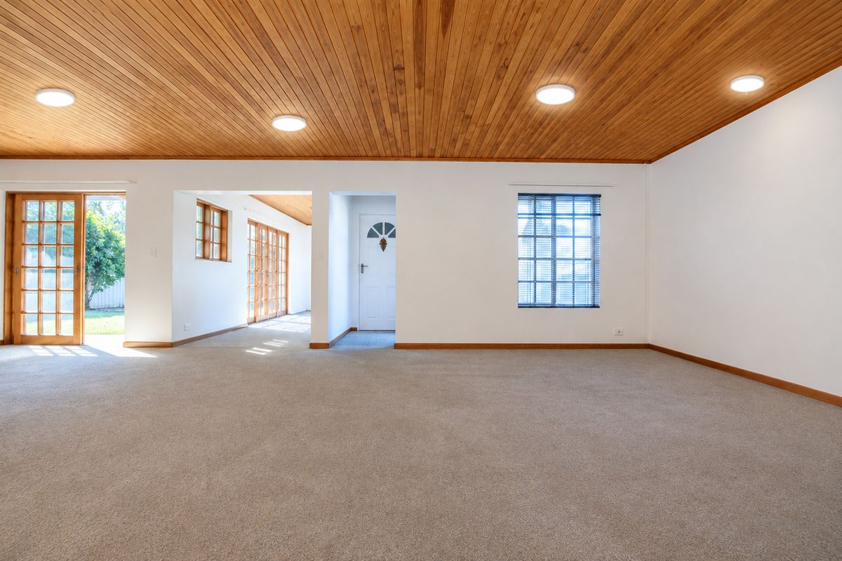 Spacious living area featuring a warm timber tongue and groove ceiling, neutral carpeting, and multiple timber-framed glass doors providing natural light and garden access.