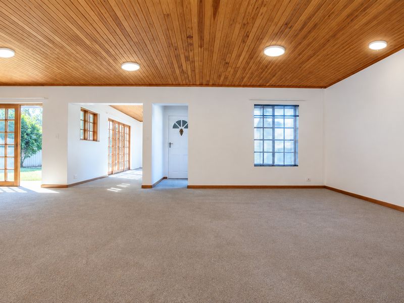 Spacious living area featuring a warm timber tongue and groove ceiling, neutral carpeting, and multiple timber-framed glass doors providing natural light and garden access.