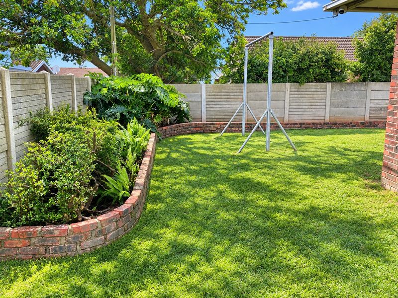A well-maintained private garden featuring a lush green lawn, established shrubbery, and decorative brick garden edging enclosed by precast concrete boundary walls.
