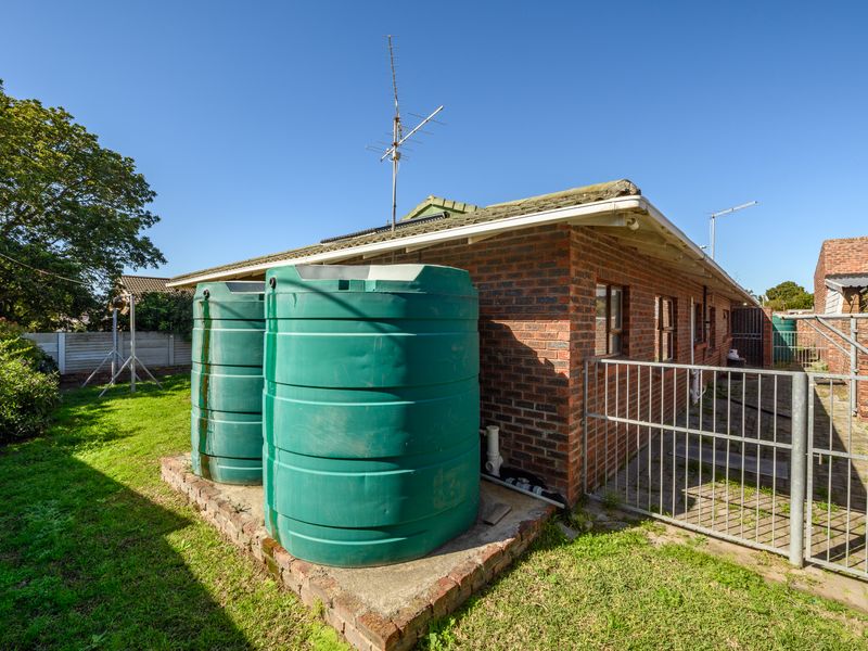 Rear exterior view of the property featuring brick construction, a paved side area with security gate, and two large water storage tanks.