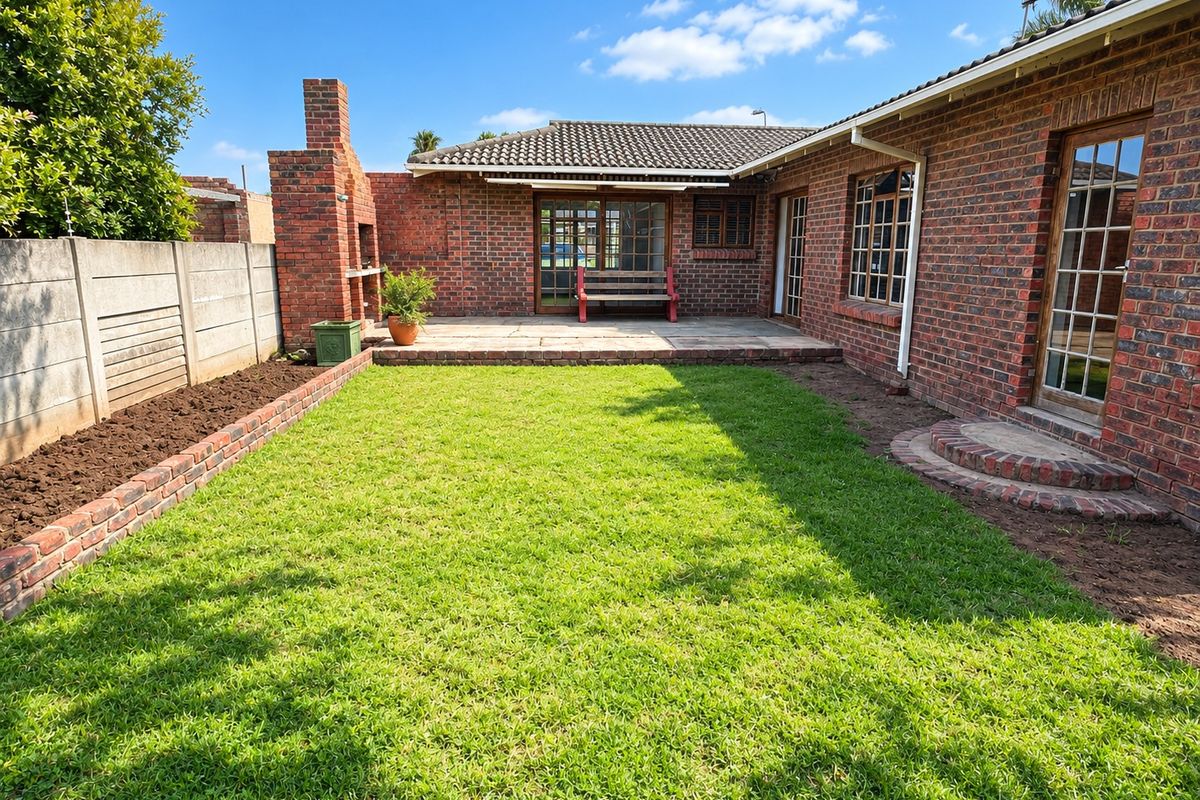 A well-maintained rear garden featuring a paved patio area, a built-in brick fireplace, and a neat lawn enclosed by brick boundary walls.