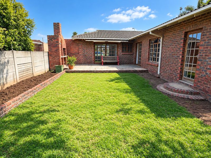 A well-maintained rear garden featuring a paved patio area, a built-in brick fireplace, and a neat lawn enclosed by brick boundary walls.