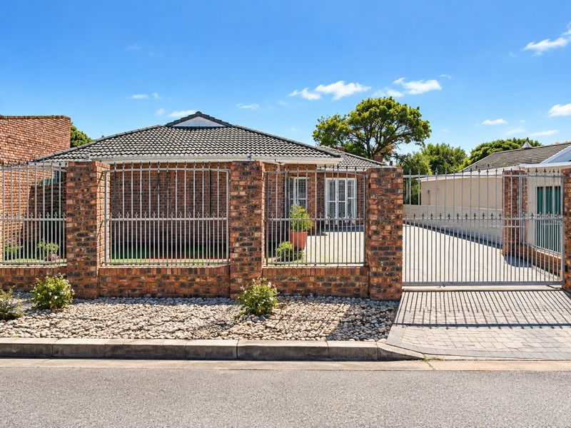 Front view of a brick-faced house featuring a secure gated entrance, paved driveway, and perimeter brick wall with metal fencing.