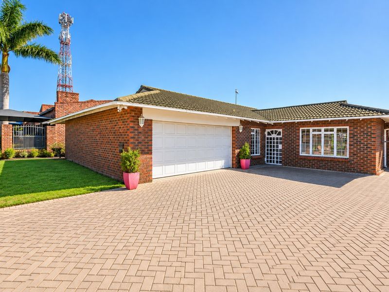 Front view of a brick house featuring a paved driveway, double garage, and well-maintained exterior finishes under a clear blue sky.