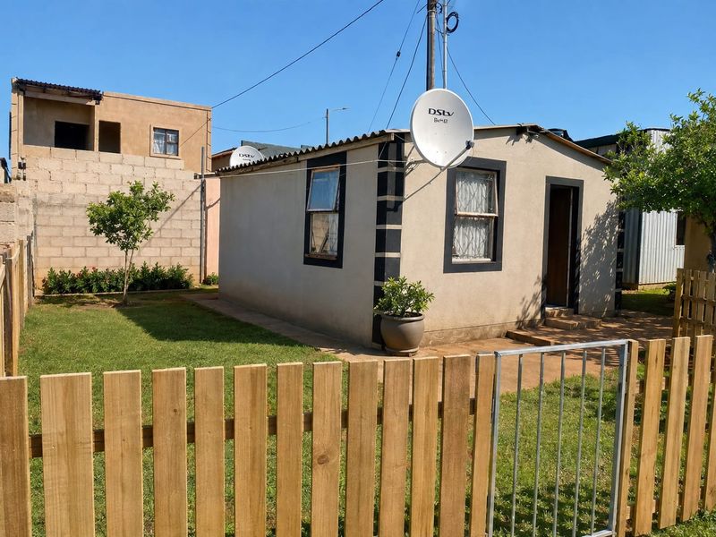 A modest single-story dwelling featuring a small front garden, timber picket fencing, and a satellite dish installation.