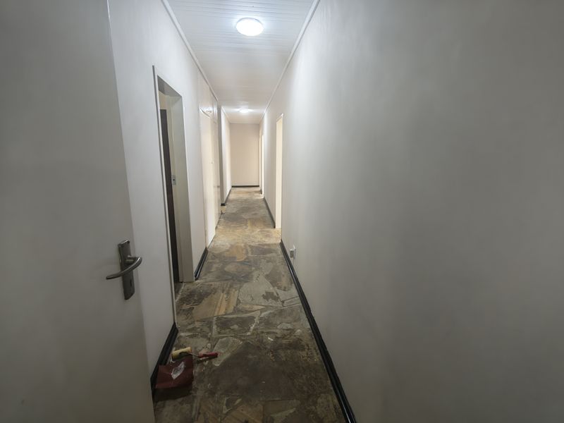 A long, empty hallway featuring stone flooring, white walls, and multiple internal door access points.
