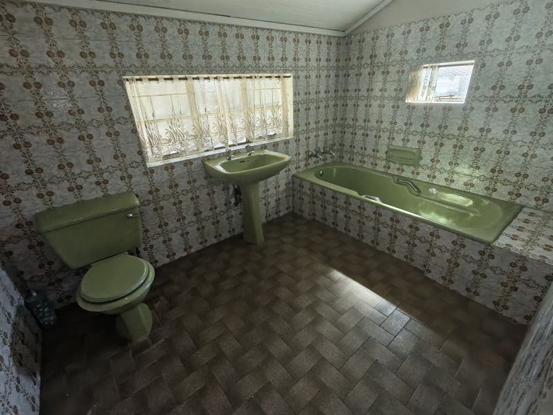 A dated bathroom featuring original green sanitaryware, including a pedestal basin, toilet, and built-in bathtub, finished with patterned wall tiles.