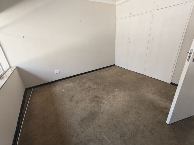 An empty bedroom featuring built-in cupboards, carpet flooring, and neutral walls, ready for renovation or staging.