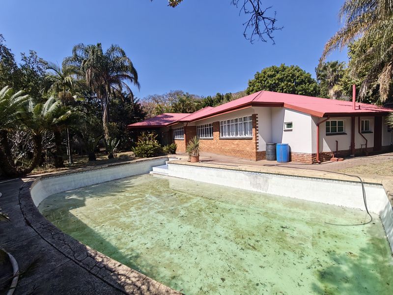 Exterior view of a house featuring a swimming pool with a brick facade and a red metal roof.