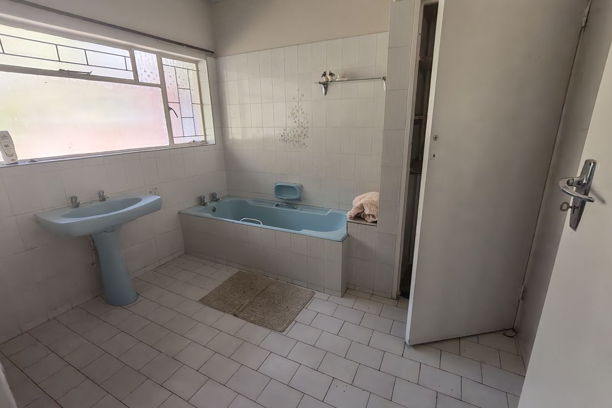 A dated bathroom featuring a blue pedestal basin and matching built-in bathtub with white wall and floor tiling.