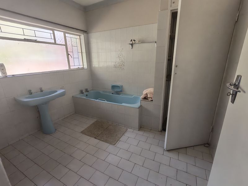 A dated bathroom featuring a blue pedestal basin and matching built-in bathtub with white wall and floor tiling.