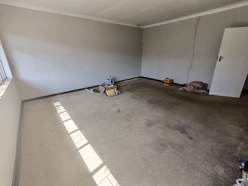 An empty living room featuring neutral walls, cove cornicing, and worn, stained carpeting in need of replacement.