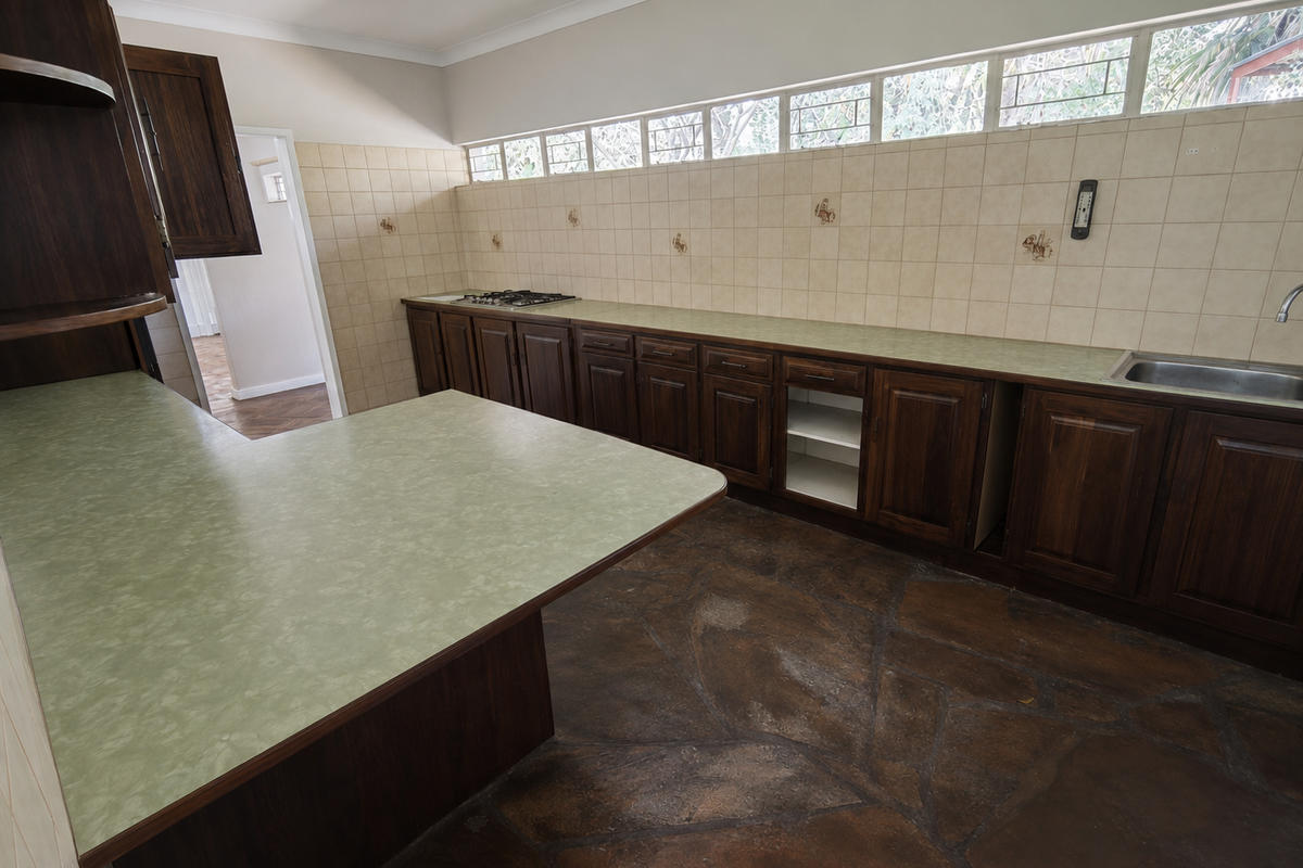 A spacious kitchen featuring dark wood cabinetry, green laminate countertops, a gas hob, and unique stone flooring, offering significant potential for a modern renovation.