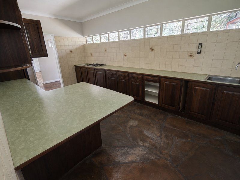 A spacious kitchen featuring dark wood cabinetry, green laminate countertops, a gas hob, and unique stone flooring, offering significant potential for a modern renovation.