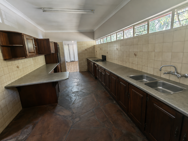 Spacious kitchen featuring extensive built-in wooden cabinetry, laminate countertops, a double stainless steel sink, and durable stone flooring.
