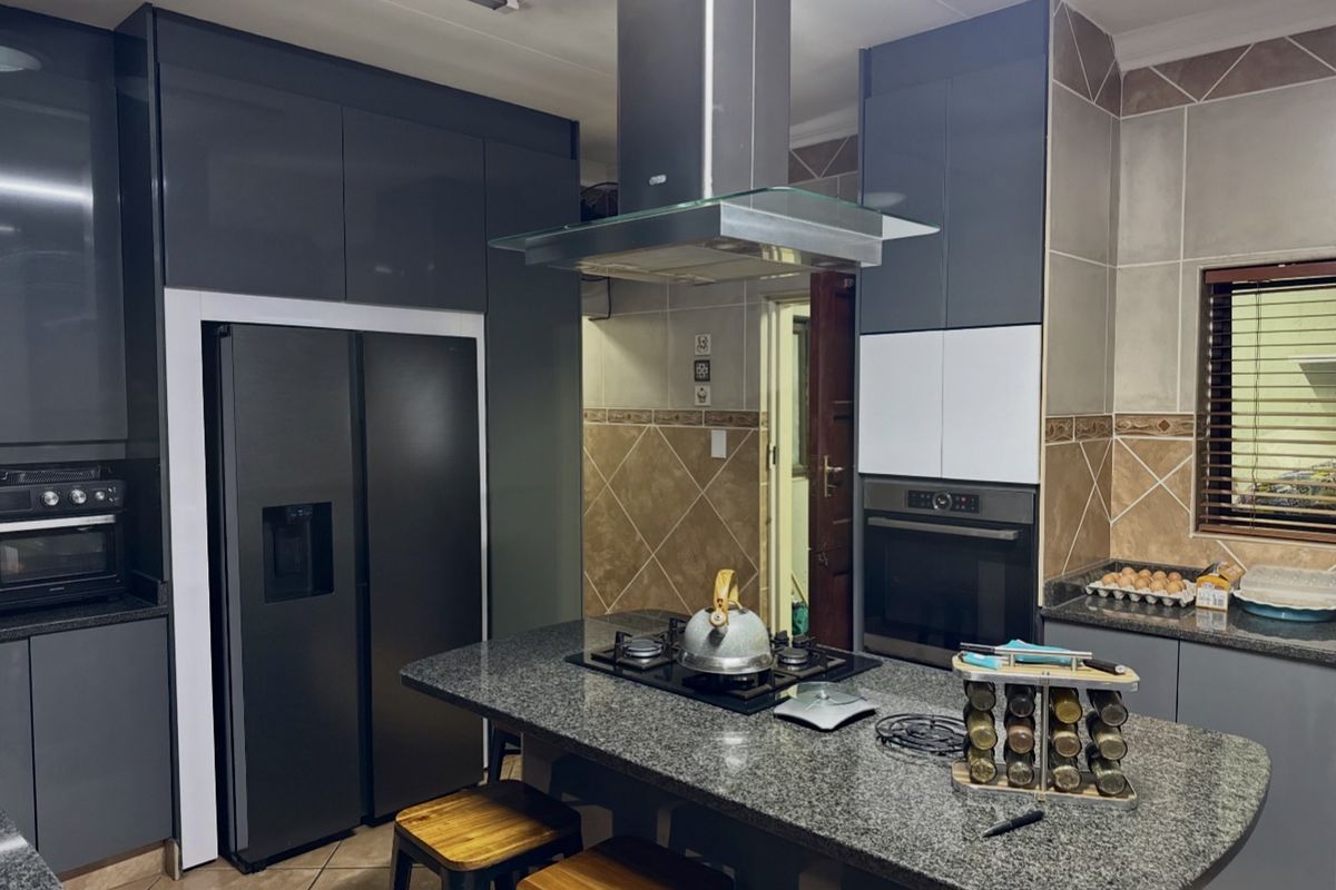 Modern kitchen featuring dark grey cabinetry, granite countertops, a central island with a gas hob, and integrated stainless steel appliances.