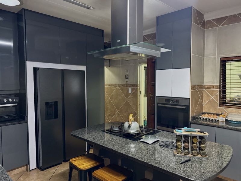 Modern kitchen featuring dark grey cabinetry, granite countertops, a central island with a gas hob, and integrated stainless steel appliances.
