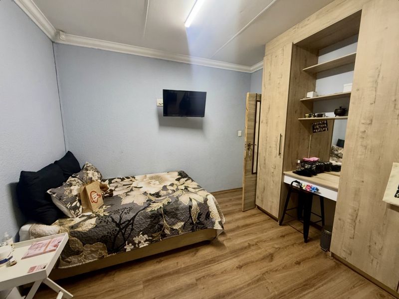 A bedroom featuring laminate flooring, coving, and a large built-in wardrobe with an integrated vanity area.