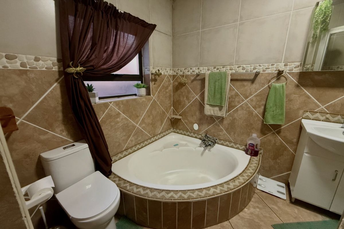 A bathroom featuring a corner bathtub, vanity cabinet, and tiled finishes throughout.