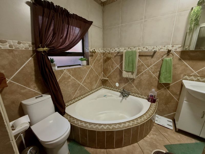 A bathroom featuring a corner bathtub, vanity cabinet, and tiled finishes throughout.