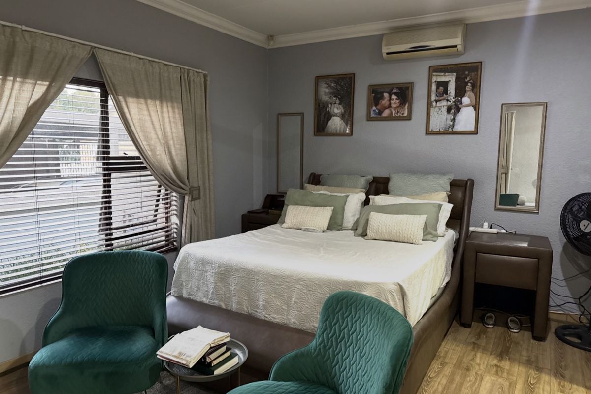 A well-maintained bedroom featuring laminate flooring, crown molding, and a wall-mounted split-system air conditioner.
