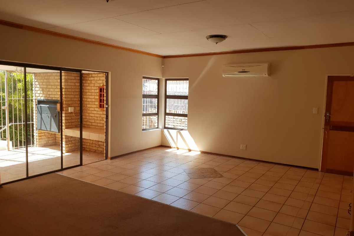 Spacious living area featuring tiled and carpeted flooring, a split-system air conditioner, and direct access to an outdoor patio with a built-in brick braai.
