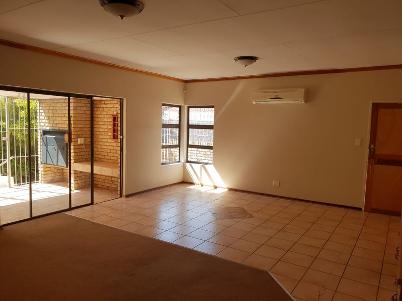 Spacious living area featuring tiled and carpeted flooring, a split-system air conditioner, and direct access to an outdoor patio with a built-in brick braai.