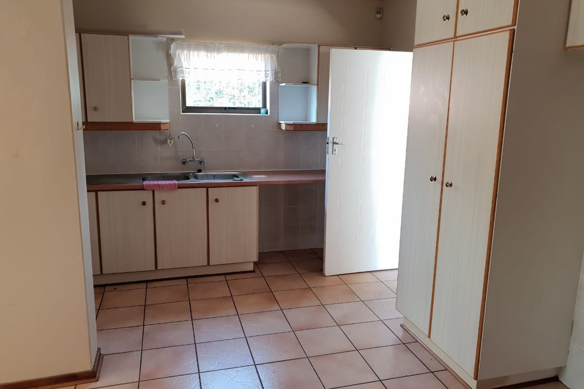 A functional kitchen featuring laminate cabinetry, a double bowl stainless steel sink, tiled splashbacks, and ample built-in storage space.