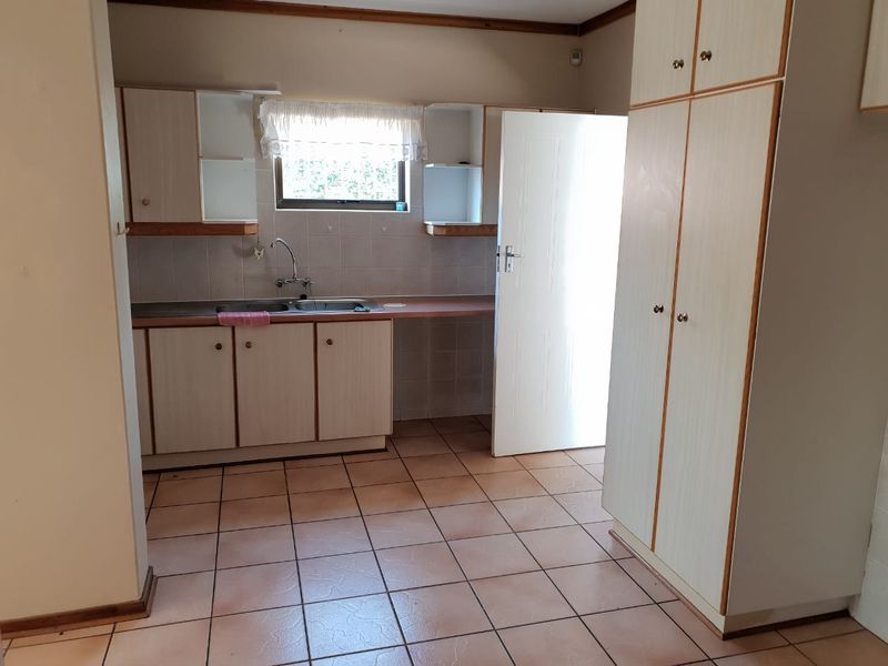 A functional kitchen featuring laminate cabinetry, a double bowl stainless steel sink, tiled splashbacks, and ample built-in storage space.