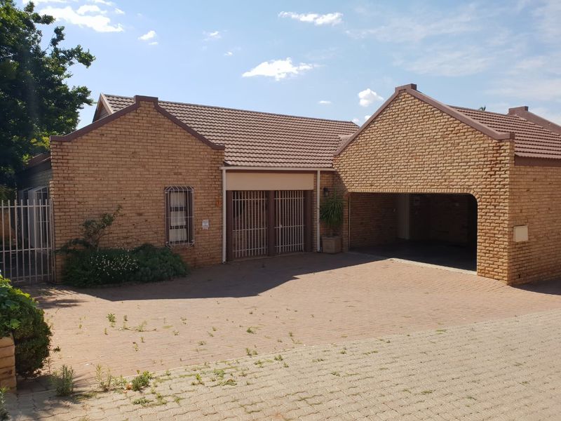 Front elevation of a face brick house featuring a double garage, paved driveway, and secure entrance with security gates.