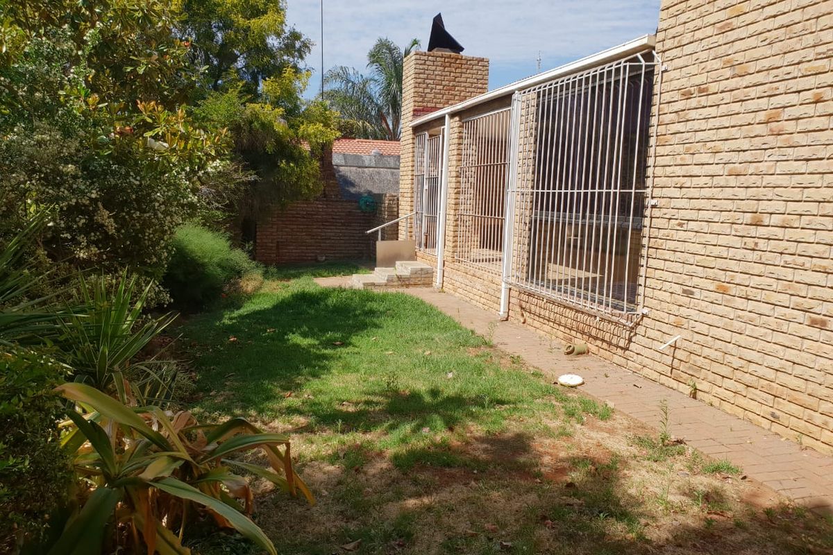 Rear exterior view of the property featuring a brick facade, security bars on windows, a brick chimney, and a garden area with a paved walkway.