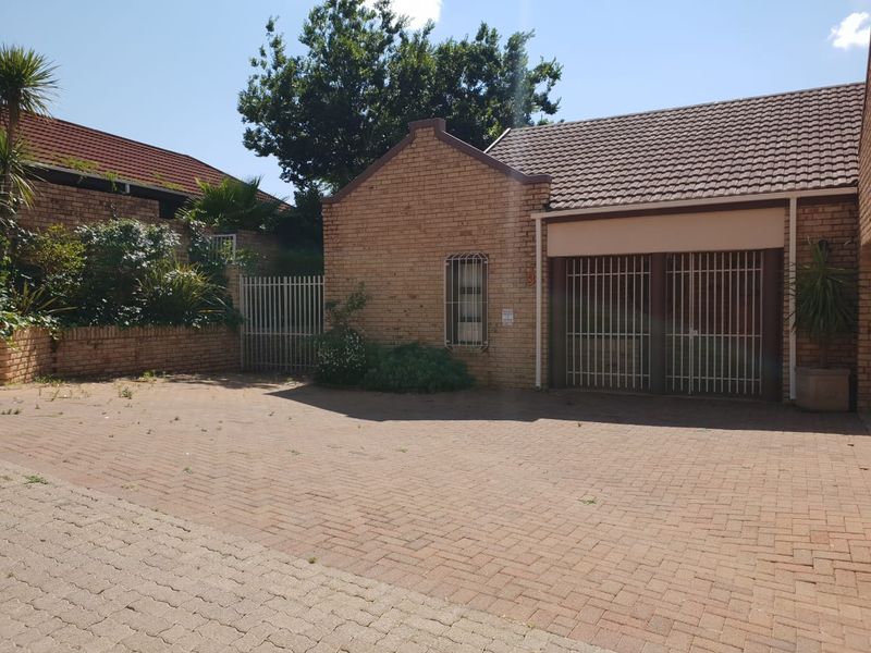 Front exterior view of the property featuring a brick facade, tiled roof, and a paved driveway with secure gated access.