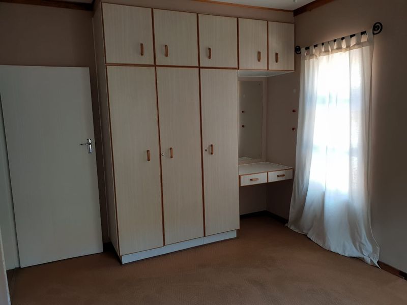 A bedroom featuring built-in wardrobes with an integrated vanity unit, carpeted flooring, and natural light from the window.