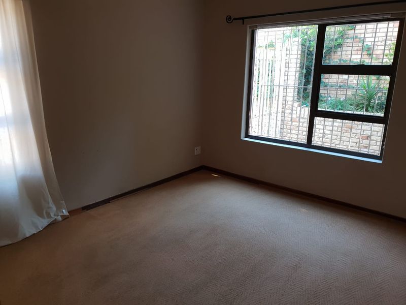 An empty bedroom featuring carpeted flooring, a window with security burglar bars, and neutral wall tones.