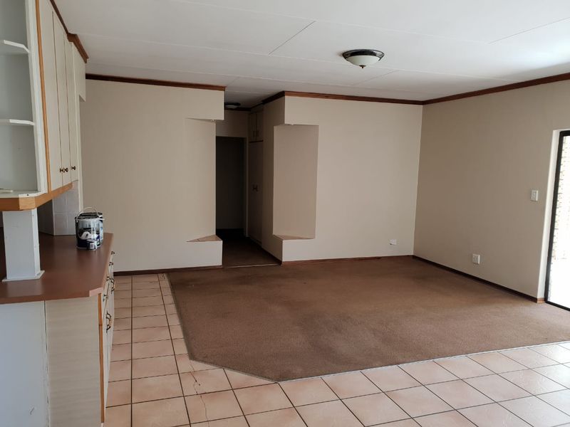 An open-plan living and kitchen area featuring tiled and carpeted flooring, built-in cabinetry, and unique wall niches, offering a blank canvas for renovation.