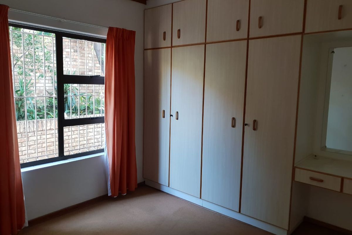 A bedroom featuring extensive built-in cupboards, a vanity area, and large windows with security bars, offering a functional and well-organized storage space.