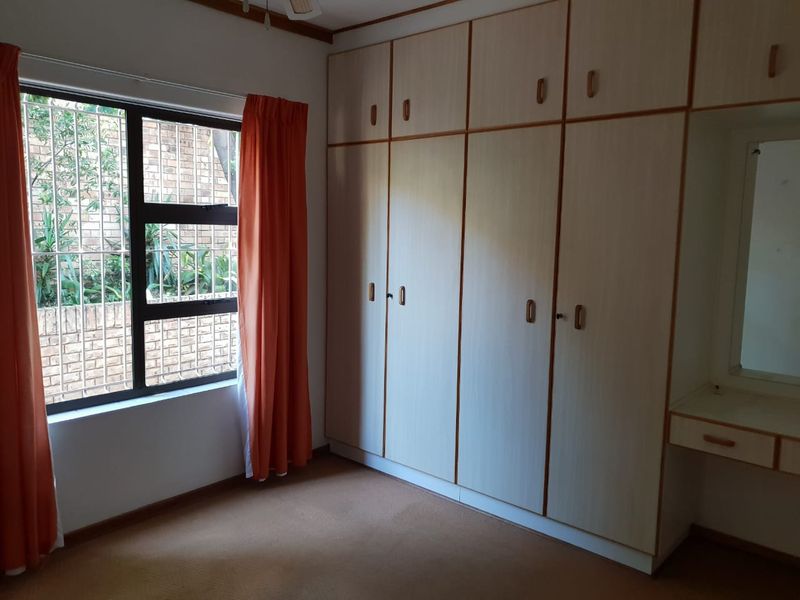 A bedroom featuring extensive built-in cupboards, a vanity area, and large windows with security bars, offering a functional and well-organized storage space.