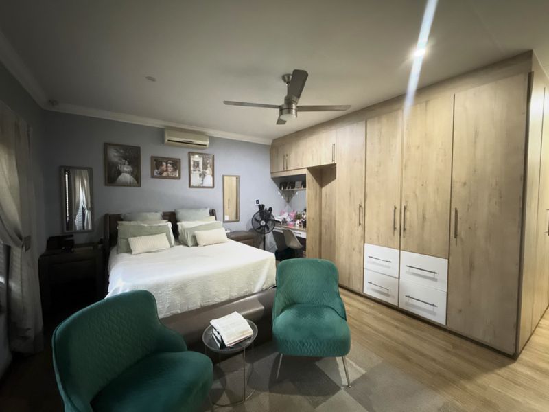 Spacious bedroom featuring extensive built-in cabinetry, integrated desk space, ceiling fan, and split-system air conditioning with modern laminate flooring.